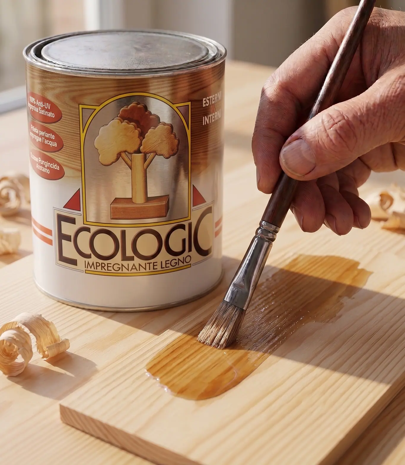 La latta di Ecologic, impregnante per legno, accanto a una mano che stende il prodotto a pennello su una tavola chiara