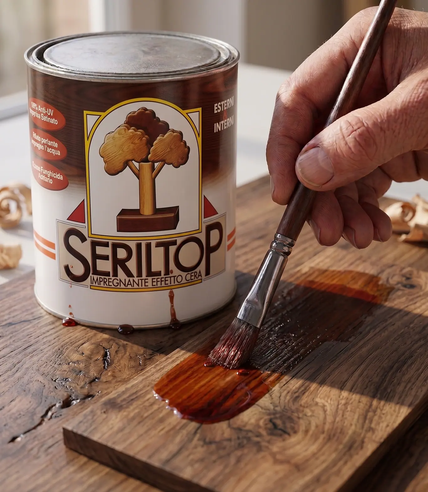 La latta di Seriltop, impregnante effetto cera, accanto a una mano che stende il prodotto a pennello su una tavola scura
