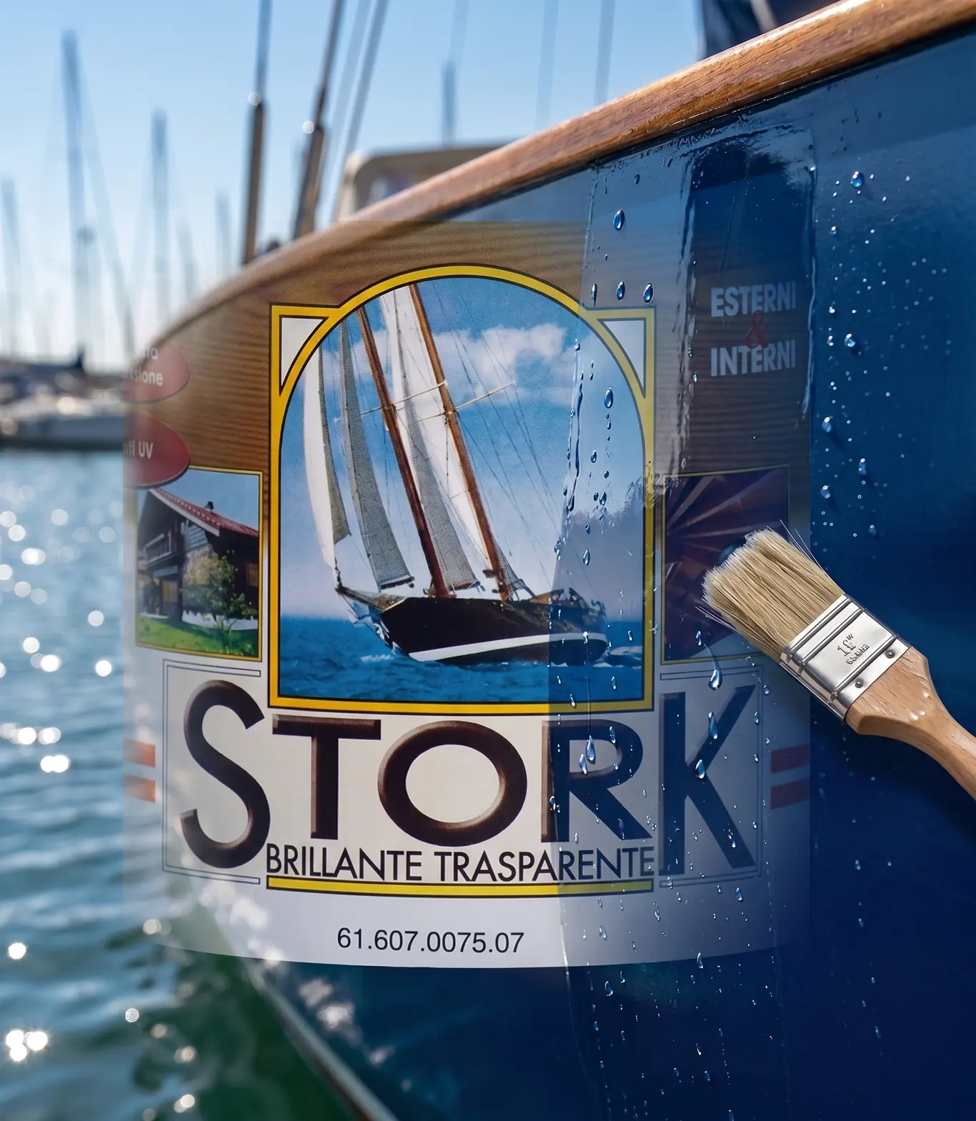 La latta di Stork Brillante Trasparente accanto a un pennello, davanti allo scafo blu di una barca, con gli alberi del porto sullo sfondo