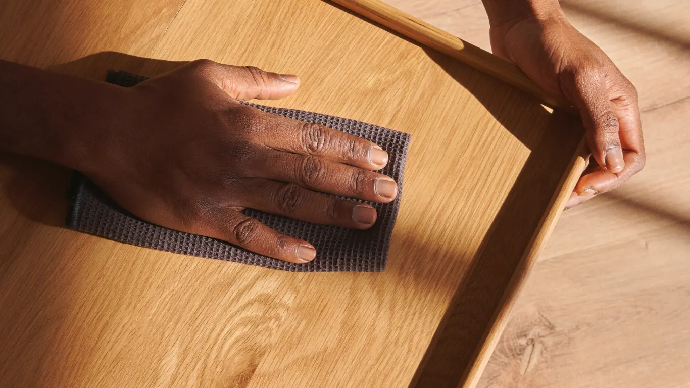 Due mani carteggiano con un tampone abrasivo il piano di un tavolo in rovere chiaro