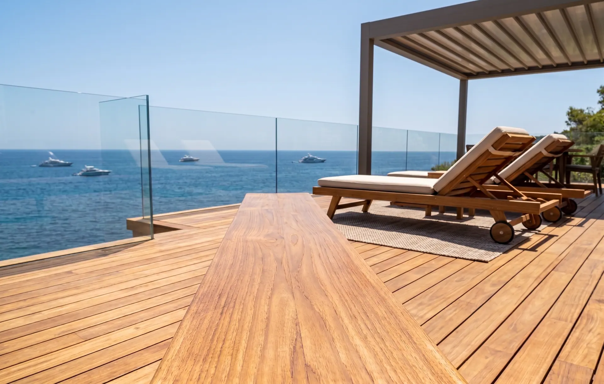 Terrazza in legno affacciata sul mare, con lettini e pergola, e le barche alla fonda sullo sfondo