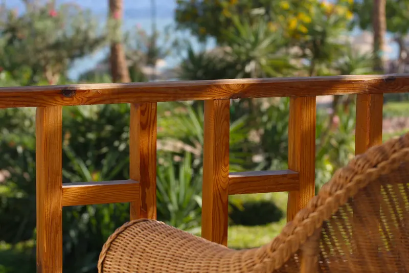 Ringhiera in legno e poltrona in vimini su una terrazza affacciata su un giardino soleggiato