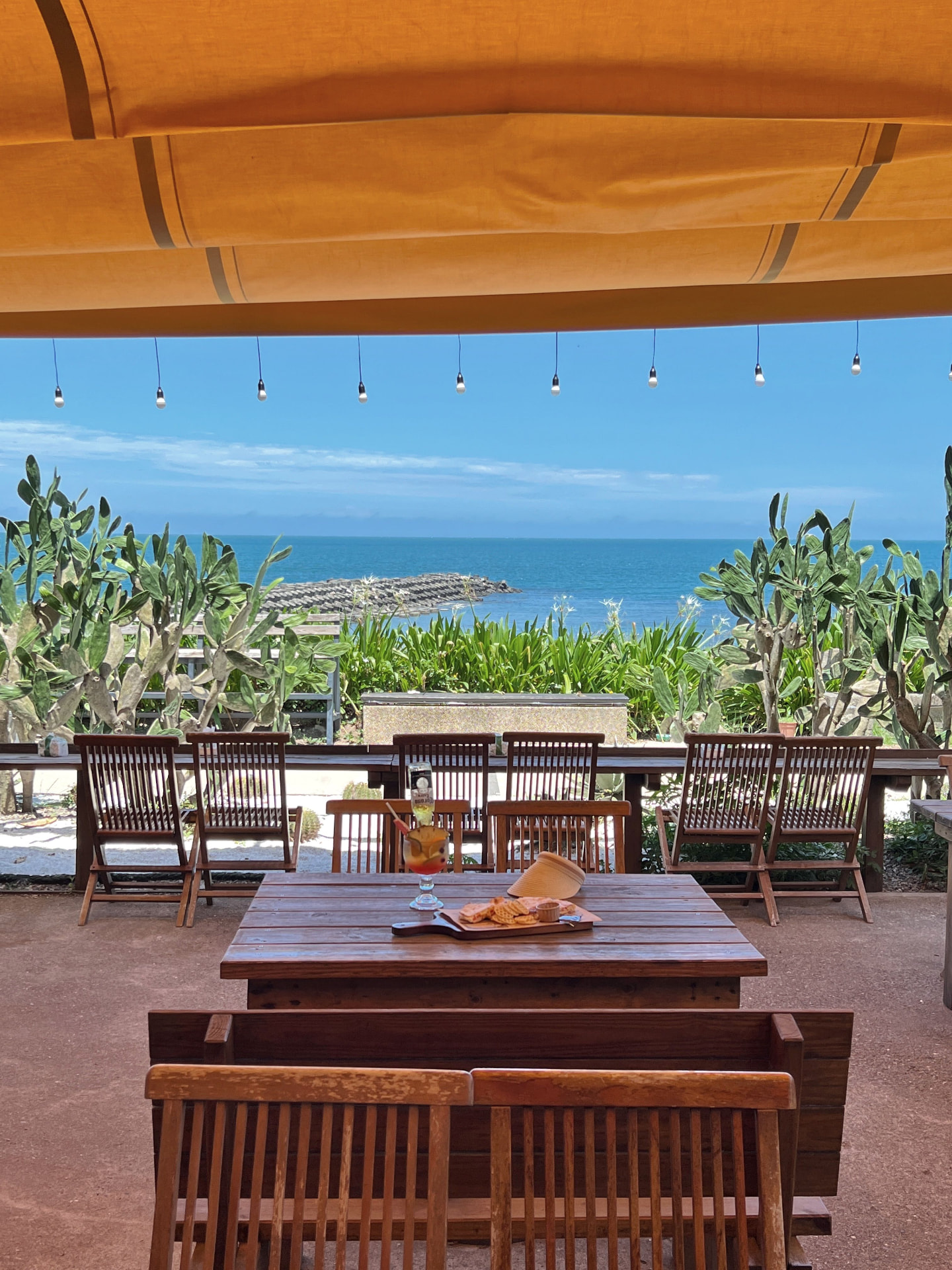 Terrazza sul mare con tavolo e sedie in legno sotto una tenda arancione