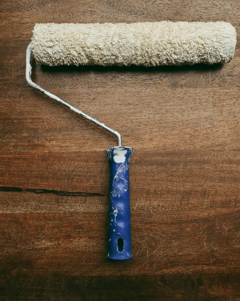 Rullo per verniciatura con impugnatura blu appoggiato su una tavola di legno scuro con venature a vista