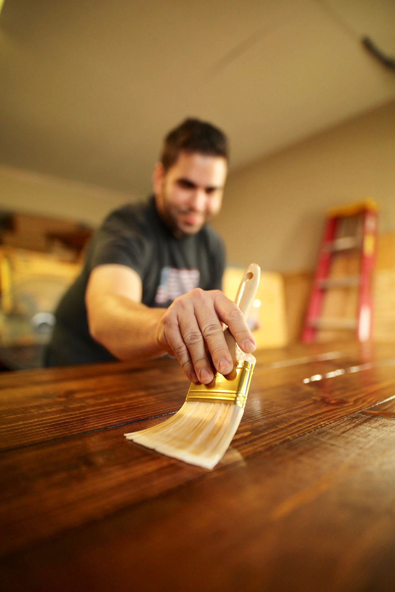 Mano che stende una mano di finitura con un pennello piatto sulle assi di un tavolo di legno scuro