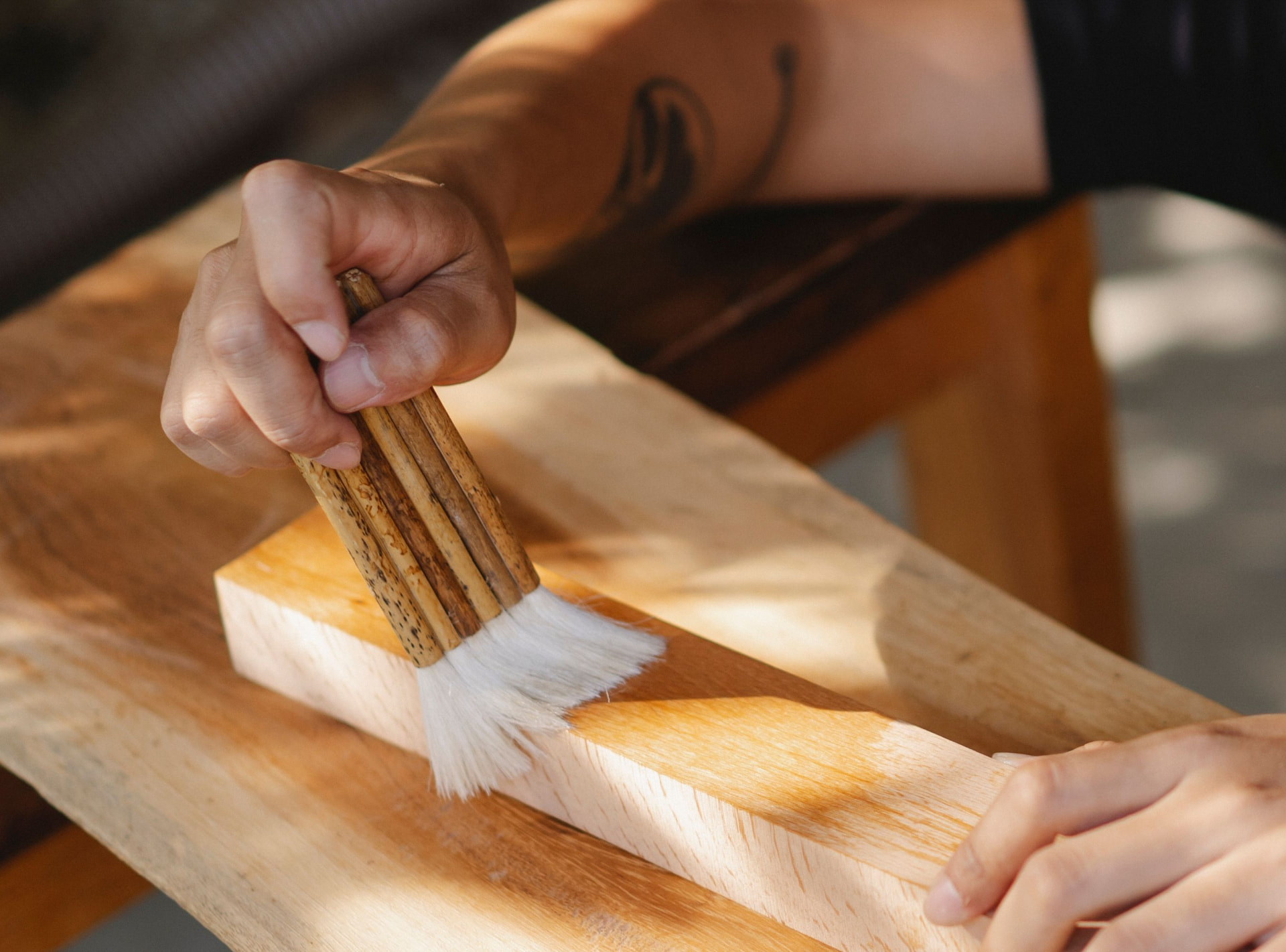 Dettaglio di una mano che passa un pennello su una tavola di legno